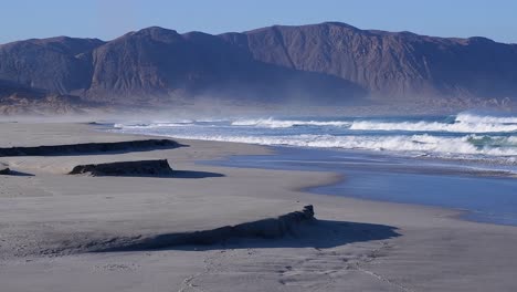 Sand-Weht-Von-Den-Bergen-Der-Atacama-Wüste-über-Die-Wellen-Des-Meeresstrandes,-Chile