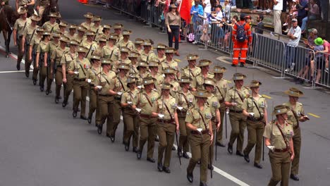 In-the-solemnity-of-Anzac-Day,-Australian-Army-troops-march-down-the-street,-some-riding-on-horseback,-participating-the-annual-parade-tradition-with-cheering-citizens-along-the-street