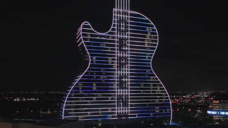 Eine-Luftaufnahme-Des-Gitarrenförmigen-Seminole-Hard-Rock-Hotel-Und-Casinos,-Das-Nachts-Mit-Neonlichtern-Beleuchtet-Wird-Und-Den-Griechischen-Unabhängigkeitstag-Feiert