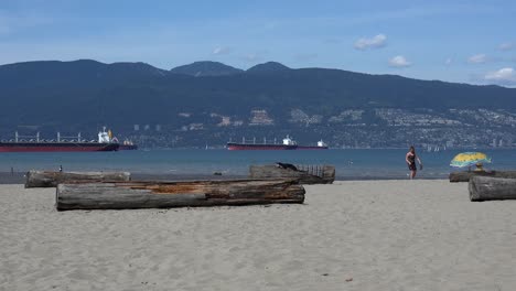 A-young-woman-plays-catch-on-Locarno-beach-Vancouver,-with-ships-and-North-Vancouver-mountains-in-the-background