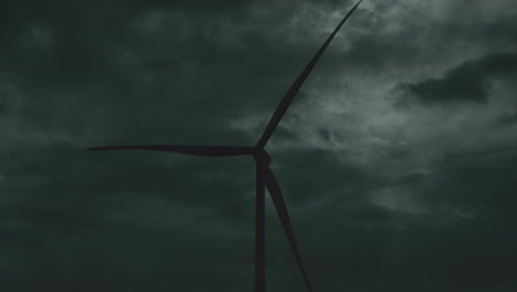 Static-medium-view-of-top-half-of-wind-turbine-silhouette-spinning-against-grey-clouds