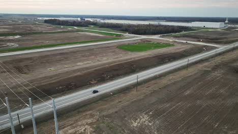 Aerial-following-vehicles-traveling-next-to-Ford's-Megacampus,-BlueOval-City-at-Sunset-in-Stanton,-TN