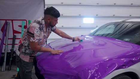 Un-Joven-Instala-Una-Envoltura-Plástica-De-Vinilo-Púrpura-En-El-Capó-De-Un-Auto-En-Una-Tienda.