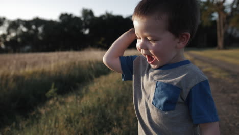 A-young,-happy-boy-playing-outside-and-throwing-dirt-in-sunset-in-cinematic-slow-motion