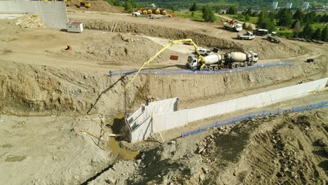 Toma-Aérea-De-Drones-De-Maquinaria-Pesada-Trabajando-En-El-Sitio-De-Construcción-De-Una-Presa-En-Las-Montañas