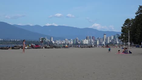 Chica-En-Bikini-Jugando-Frisbee-En-La-Playa-De-Locarno-Con-El-Horizonte-De-Vancouver-Y-El-Parque-Stanley-Al-Fondo