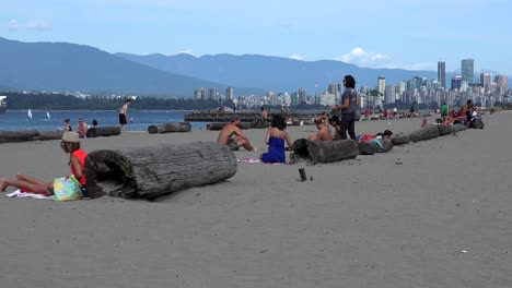 Strand-Von-Locarno-Mit-Einer-Gruppe-Junger-Leute-Im-Gespräch-Mit-Blick-Auf-Die-Stadt-Vancouver-Und-Den-Stanley-Park-Im-Hintergrund