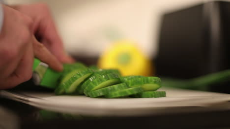 Cutting-up-Cucumber-at-home-on-White-chopping-board,-with-green-knife