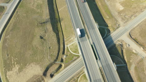 Bird's-eye-view-of-a-highway-intersection-with-overpass-and-underpass,-featuring-sparse-traffic-and-surrounding-undeveloped-land