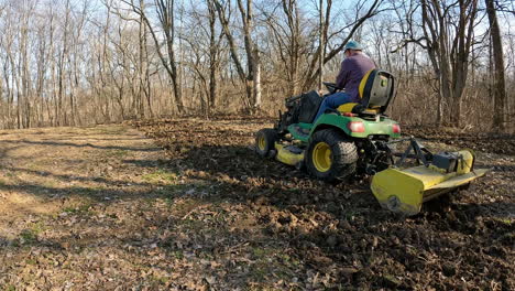 Man-drives-a-utility-tractor-to-tow-a-rototiller-to-turn-soil-to-prepare-a-deer-food-plot-for-planting-near-woods-and-a-field