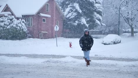 woman-running-outdoors-during-a-snowstorm-around-a-residential-street,-slow-motion-footage