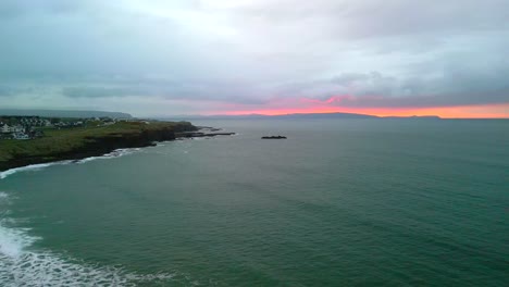 A-red-sky-at-night,-with-moody-clouds-punctuating-the-crashing-waves-on-Portrush-West-Strand-beach