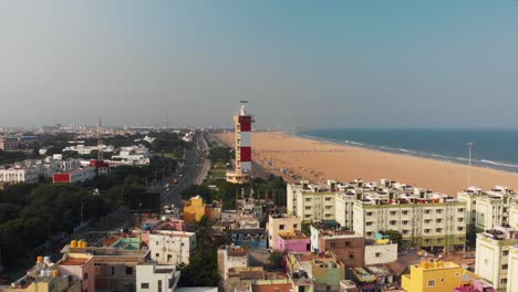 Aerial-Tilt-Up-Over-Buildings-With-Chennai-Marina-Lighthouse-Beside-Coastal-Beach-In-India