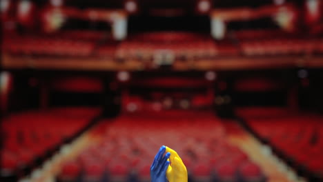 Blue-And-Yellow-Tiny-Fingerhandd-Finger-Puppet-Toys-Clapping-Against-Blurry-Theater-Background