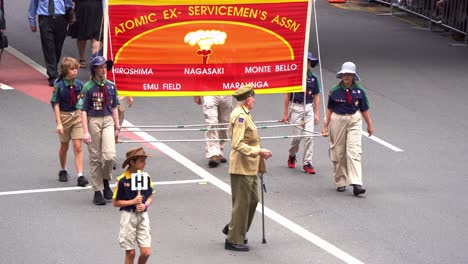 Cheerful-sergeant-from-the-Atomic-Ex-Servicemen's-Association-walking-down-the-street,-waving-at-the-cheering-crowds