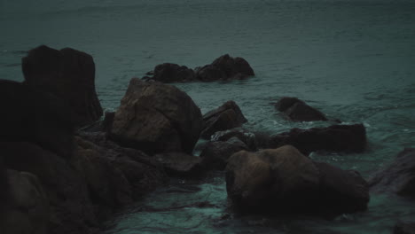 Medium-shot-of-rocky-coastal-region-on-stormy-grey-day-as-water-swirls-around-small-boulders