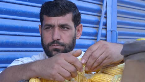 Hombre-Trabajando-En-Un-Bazar-En-La-Calle-Saddar-De-Karchi-Separando-La-Mazorca-De-Maíz