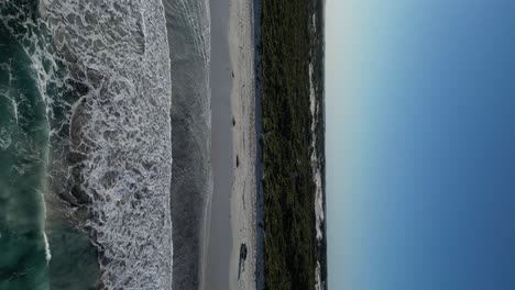 Drone-flight-over-clear-ocean-water-and-sandy-beach-with-driving-4x4-car