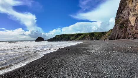 People-walking-on-shingle-beach-older-high-cliffs-on-a-spring-day-at-Ballydwane-Copper-Coast-in-Waterford-Ireland