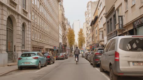 Tracking-wide-of-Antwerp-cyclist-biking-through-and-empty-street-full-of-parked-cars