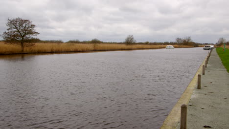 shot-looking-up-the-river-Bure-with-a-white-Norfolk-Broads-cruisers-boat-passing-moored-boats