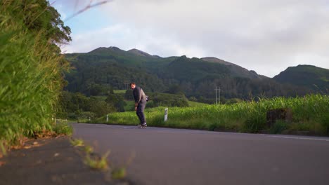 Man-rides-his-skateboard-in-the-road-with-mountains-in-the-background