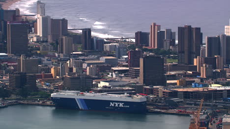 Aerial-shot-of-a-RORO-ship-in-Durban-Harbour,-zooming-out-to-a-wide-shot-of-the-city