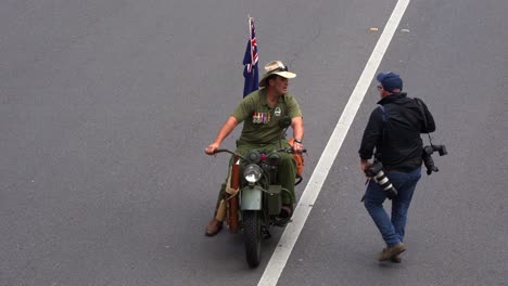 Un-Hombre-Viaja-En-Una-Motocicleta-Antigua-Con-La-Bandera-Nacional-Australiana-En-La-Parte-Trasera,-Moviéndose-Por-La-Calle-Durante-El-Desfile-Del-Día-De-Anzac