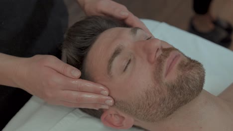 A-man-on-a-massage-table-gets-his-temples-massaged-by-the-masseuse