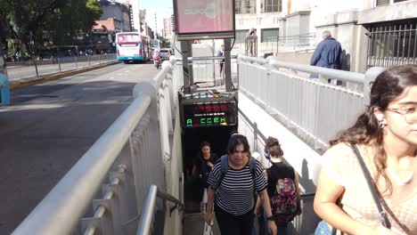 Beautiful-latin-women-go-outside-underground-metro-station-upstairs-buenos-aires-city-argentina-flores-neighborhood-rivadavia-avenue-in-autumn-daylight,-traffic-driving-by