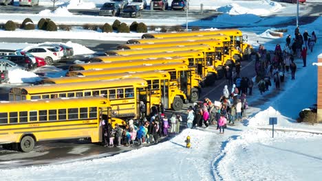 Niños-De-Escuela-Primaria-Abordando-Autobuses-Escolares-Amarillos-Durante-La-Salida-Temprana-Por-Tiempo-De-Nieve