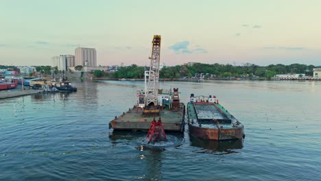 Greifbagger-Sammelt-Und-Kippt-Flusssediment-Auf-Ein-Lastkahn-Auf-Dem-Rio-Ozama