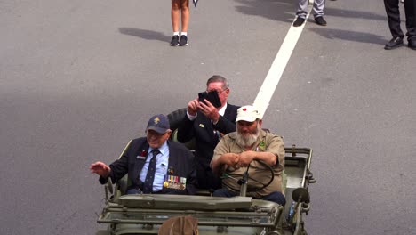 Senior-veteran-riding-on-military-Willys-jeep,-driving-down-the-street-during-Anzac-Day-parade,-handheld-motion-close-up-shot