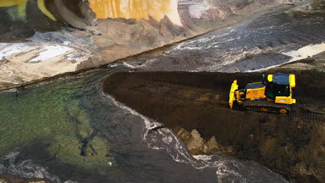 Aerial-zoom-in-shot-yellow-bulldozer-using-shovel-to-drag-new-soil-on-land-construction