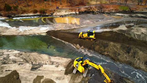 Aerial-dolly-right-shot-of-excavator-removing-sediment-from-a-creek-bottom-and-bulldozer-driving-backwards-on-dirt-road