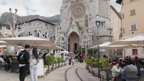 Animada-Terraza-De-Un-Café-En-Sóller,-Mallorca,-Con-Una-Iglesia-Histórica-Como-Telón-De-Fondo