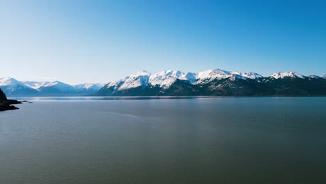 AERIAL:-Mountains-in-Alaska-next-to-Lake-with-Blue-Sky-and-Snowy-Peaks