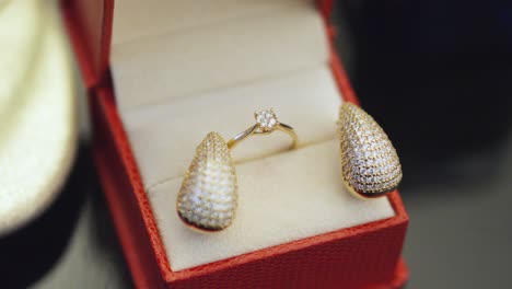 Closeup-of-diamond-earrings-and-gold-ring-inside-a-red-box
