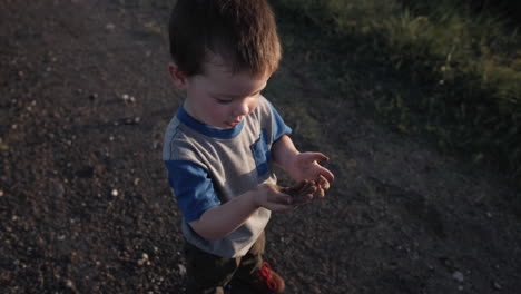 A-young,-happy-boy-playing-outside-and-throwing-dirt-in-sunset-in-cinematic-slow-motion