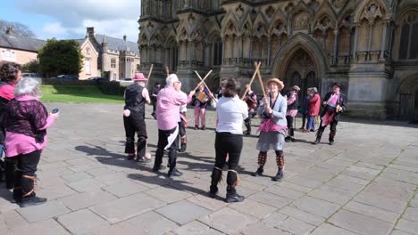 Morris-dancers-with-shin-bells-and-sticks-dancing-to-traditional-English-folk-music-in-public-performance-at-Wells-Cathedral-in-Somerset,-UK