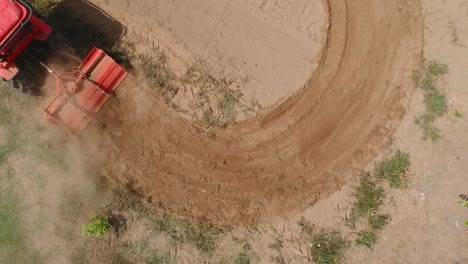 Shooting-from-drone-flying-over-tractor-with-harrow-system-plowing-ground-on-cultivated-farm-field,-pillar-of-dust-trails-behind,-preparing-soil-for-planting-new-crop,-agriculture-concept,-top-view