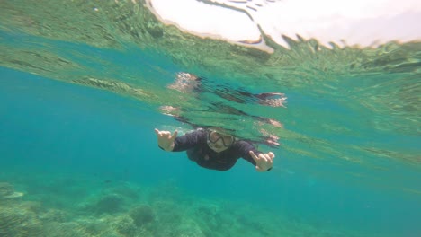 Woman-Snorkeler-Waving-At-Camera-While-Swimming-Under-Sea-Surface