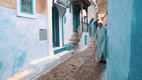 Anciano-Marroquí-Con-Ropa-Tradicional-Caminando-Por-Una-Hermosa-Calle-En-Chefchaouen,-Marruecos