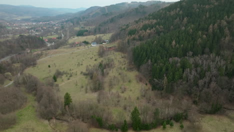 Aerial-view-of-Jedlina-Zdrój,-showcasing-the-rustic-charm-of-this-mountain-village-in-Poland,-with-its-rolling-hills,-dense-patches-of-evergreen-trees,-and-scattered-houses