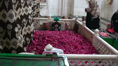 Mujer-Rezando-En-Una-Tumba-Cubierta-De-Flores-En-Gujrat,-Pakistán