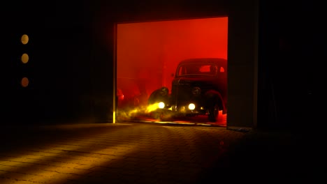 A-black-vintage-car-drives-out-of-a-garage-at-night