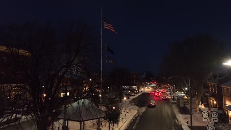 Stadtplatz-Mit-Amerikanischer-Flagge-Und-Schneebedeckten-Geschäften-In-Der-Nacht