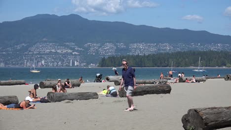 Ocean-beach-with-sunbathers-and-swimmers,-and-a-man-walking-by