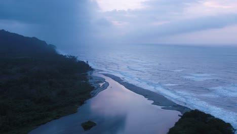 Luftaufnahme-Von-Wellen,-Die-An-Die-Küste-Krachen,-Mit-Grünen-Bergen-Auf-Der-Linken-Seite,-Vor-Einem-Düsteren-Himmel-Mit-Wolken-In-Kolumbien
