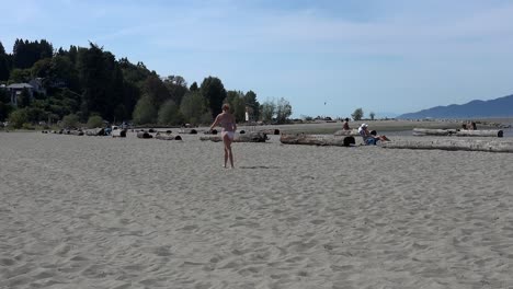 A-young-woman-in-a-bikini-on-a-beach-picks-up-a-frisbee